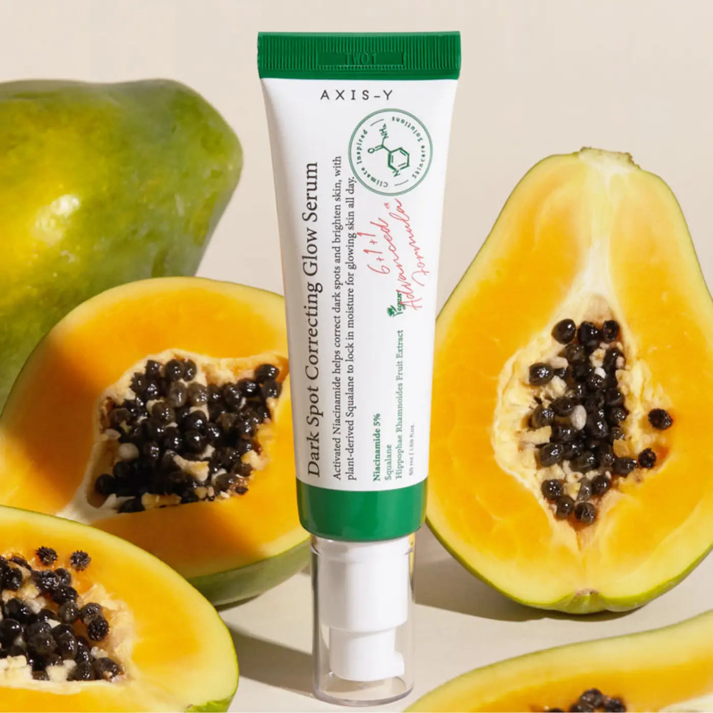 A white and green tube of axis-y dark spot correcting glow serum with pump dispenser surrounded by sliced papayas